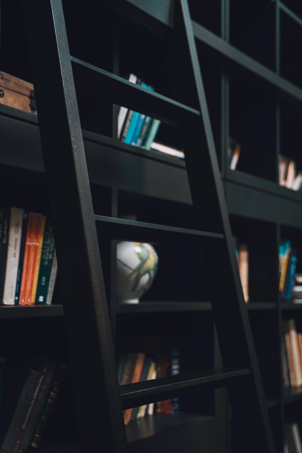 A library bookshelf features books, a patterned vase, and trunk.